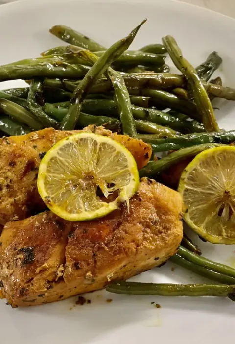 Lemon garlic green beans with chicken thighs on a white plate, topped with roasted lemon slices