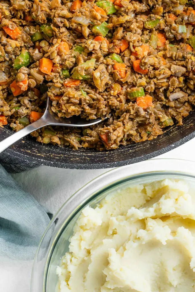 Lentil and vegetable filling in a skillet next to a bowl of mashed potatoes