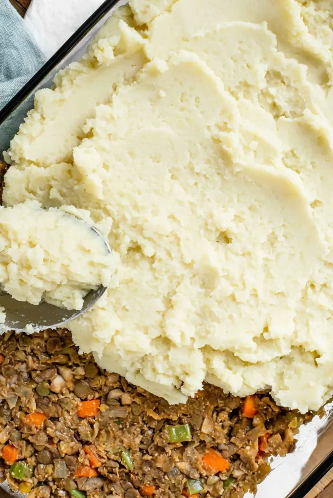 Mashed potatoes being spread over the lentil filling
