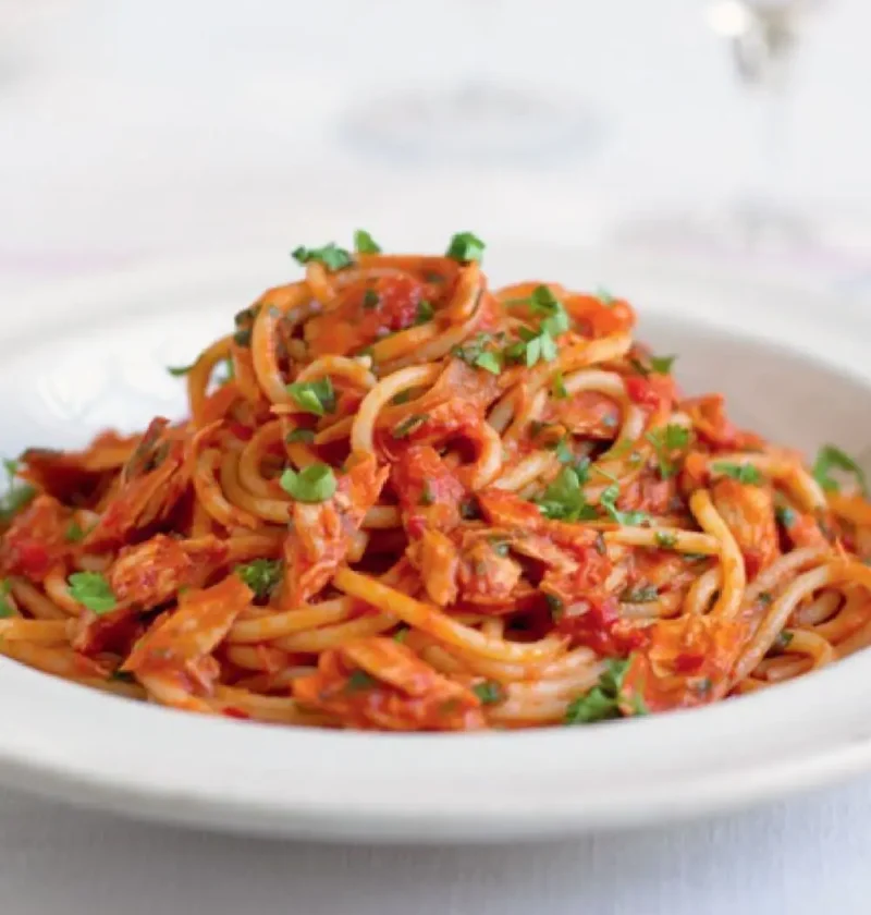 Linguine with tuna fish sauce in a white bowl, topped with chopped parsley
