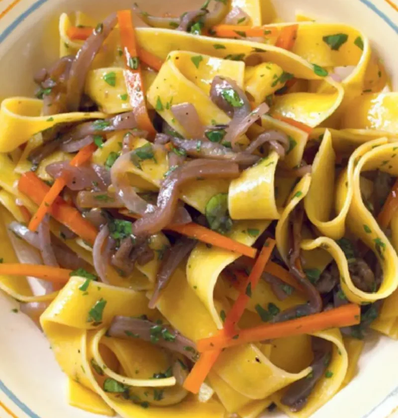 Maltagliati with eggplant sauce, wide pasta ribbons with onion and carrot strips and parsley in a bowl