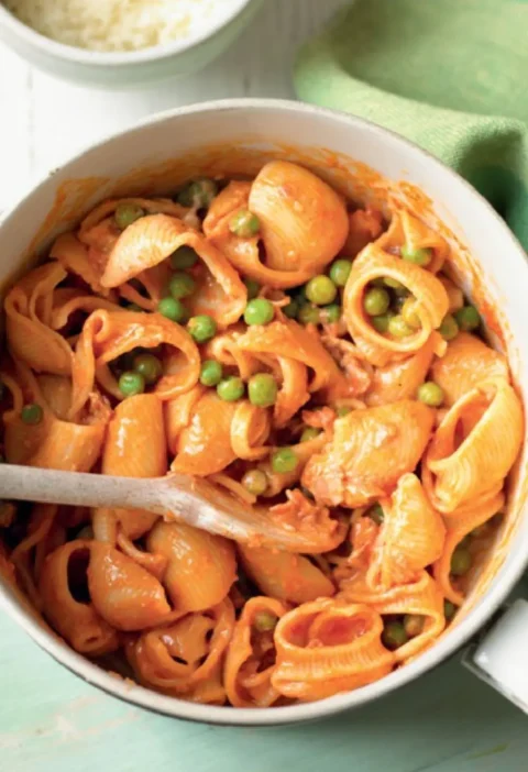 Marille with peas, shell pasta in a creamy tomato sauce with green peas in a white pot with a wooden spoon