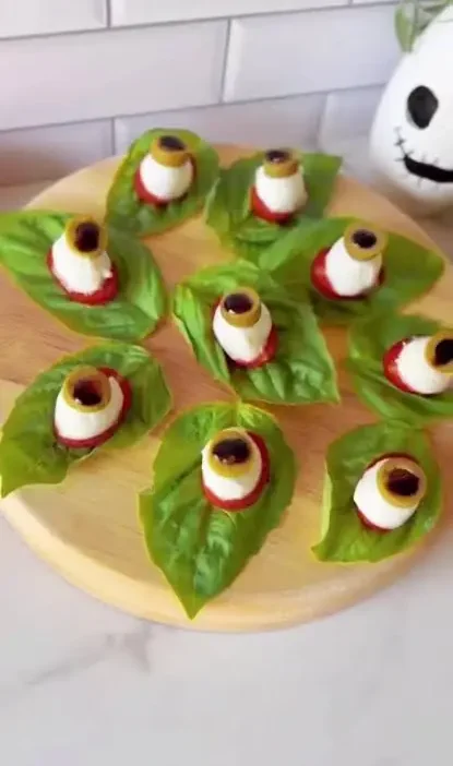 Mozzarella eyeball caprese on basil leaves with tomato and olive slices on a wooden platter