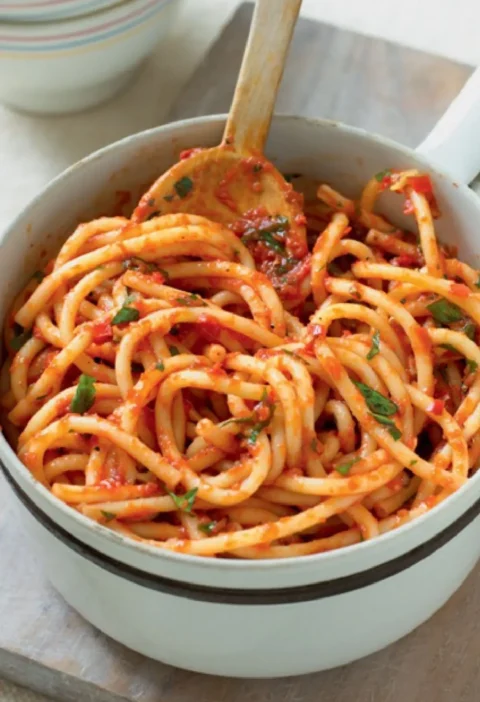 Neapolitan-style macaroni in a white pot with a wooden spoon, thick pasta strands coated in tomato sauce and parsley