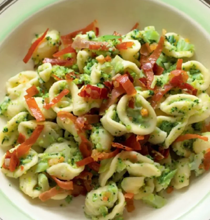 Orecchiette with Broccoli in a green-rimmed bowl topped with crispy strips of speck