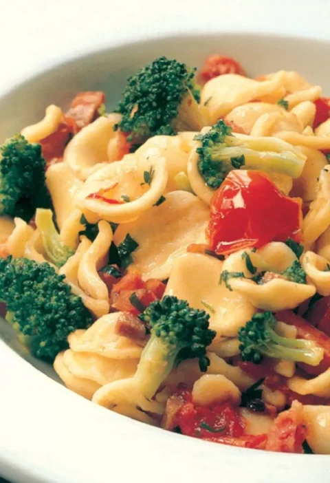 Orecchiette with broccoli florets, prosciutto and cherry tomatoes in a white bowl