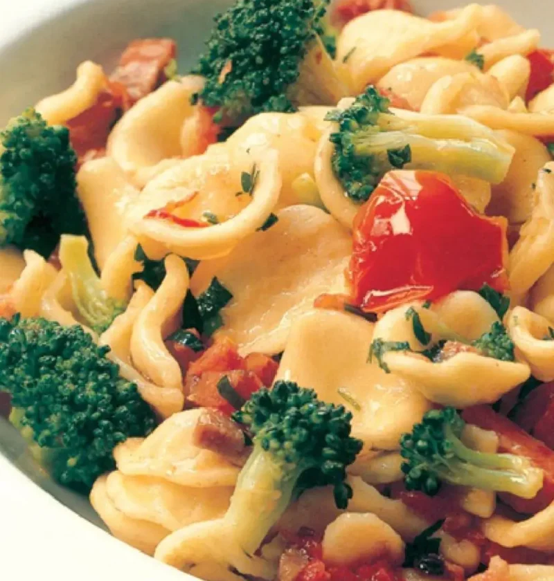 Orecchiette with broccoli florets, prosciutto and cherry tomatoes in a white bowl