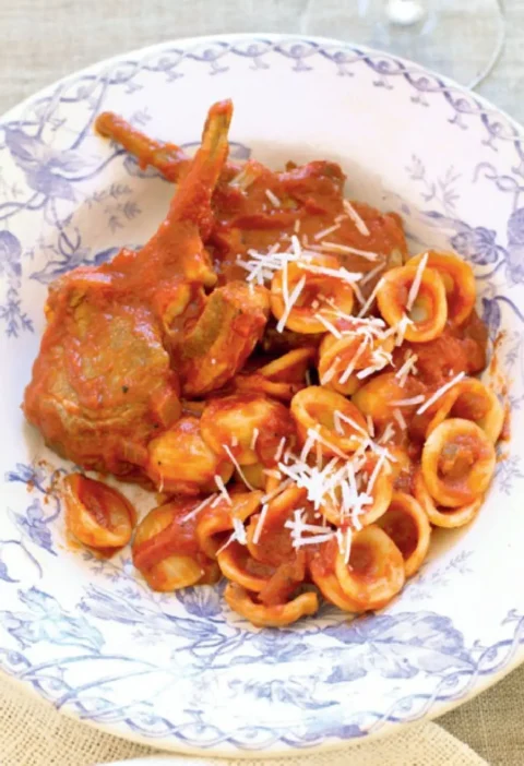 Orecchiette with lamb ragout and a lamb cutlet in a blue and white bowl topped with grated pecorino
