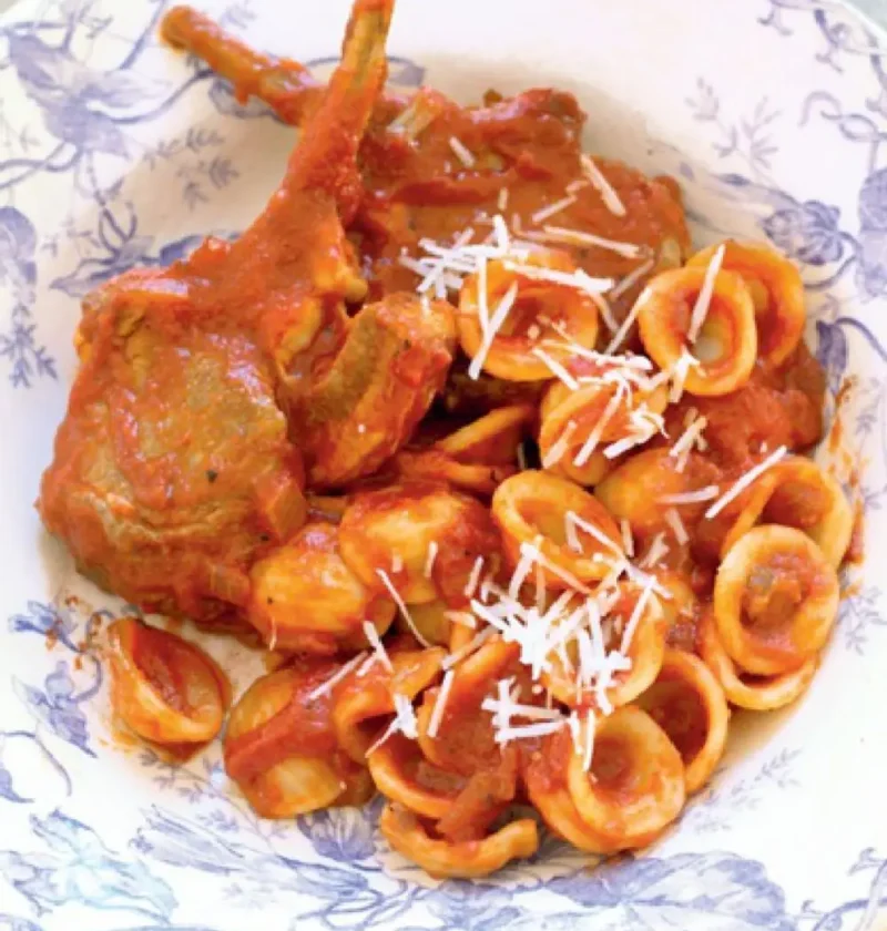 Orecchiette with lamb ragout and a lamb cutlet in a blue and white bowl topped with grated pecorino
