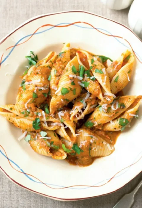 Orecchioni with piquant sauce in a white bowl, topped with grated pecorino and chopped parsley