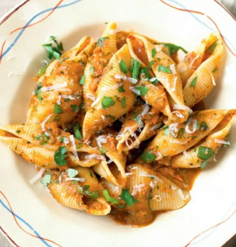 Orecchioni with piquant sauce in a white bowl, topped with grated pecorino and chopped parsley