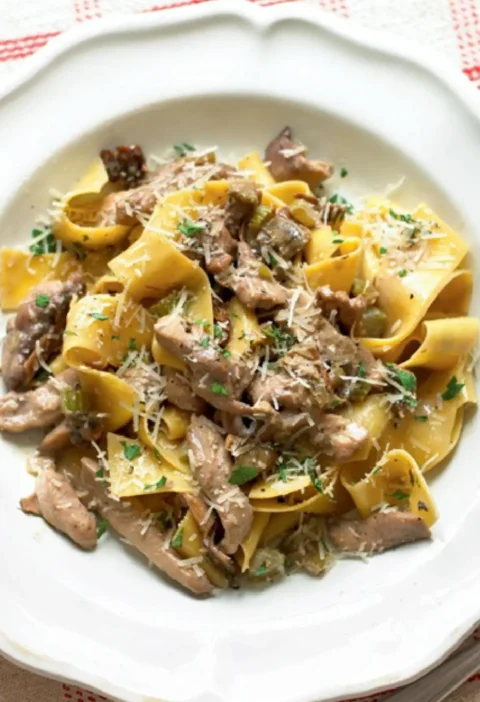 Pappardelle with quail sauce on a white plate topped with grated Parmesan and parsley