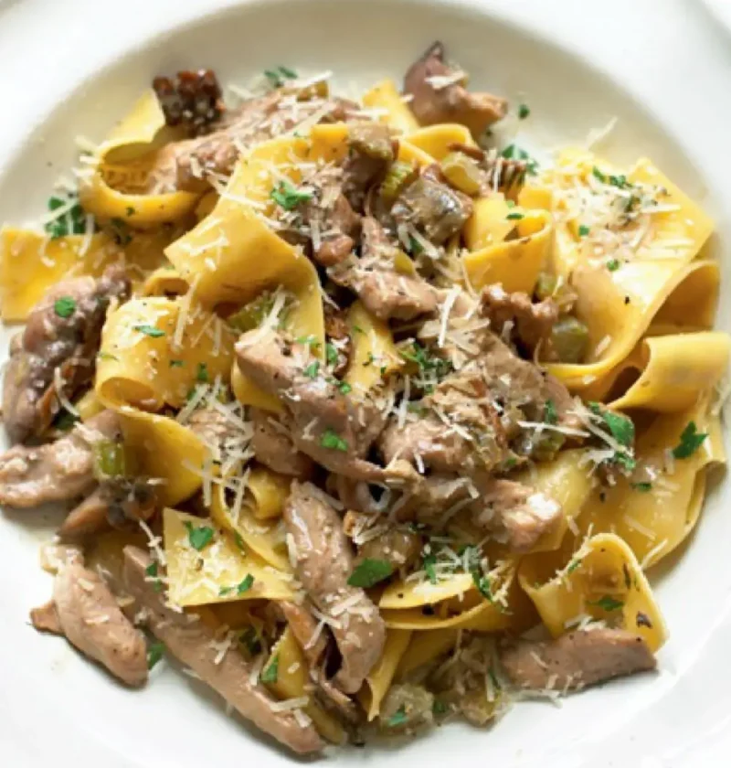 Pappardelle with quail sauce on a white plate topped with grated Parmesan and parsley