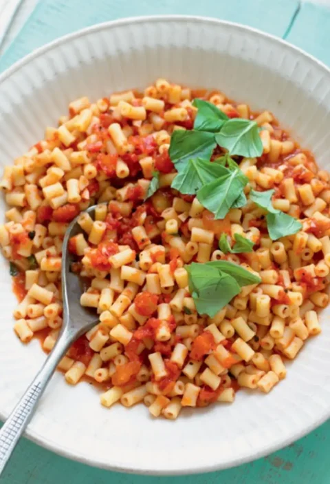 Pasta salad al fresco with small tube pasta in tomato sauce and fresh basil leaves in a white bowl