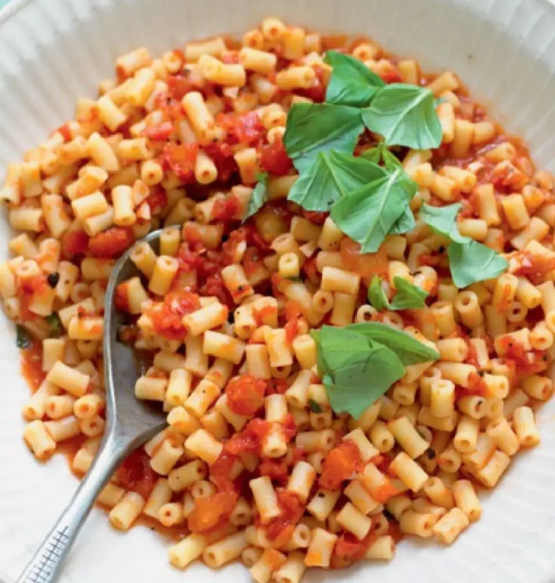 Pasta salad al fresco with small tube pasta in tomato sauce and fresh basil leaves in a white bowl