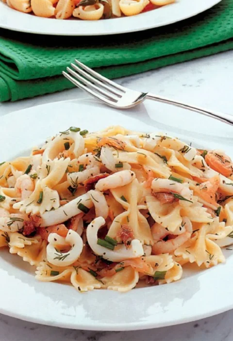Pasta salad with fish on a white plate with farfalle, squid rings, shrimp, smoked salmon and fresh chives