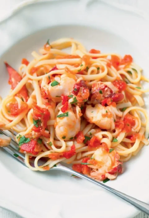 Pasta with lobster: linguine with chunks of lobster, chopped tomato and parsley on a white plate