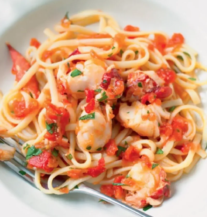 Pasta with lobster: linguine with chunks of lobster, chopped tomato and parsley on a white plate