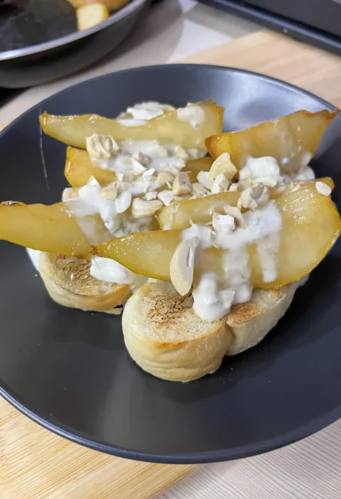 Pear and gorgonzola bruschetta on a dark plate with golden pear wedges, gorgonzola sauce and cashews on toast