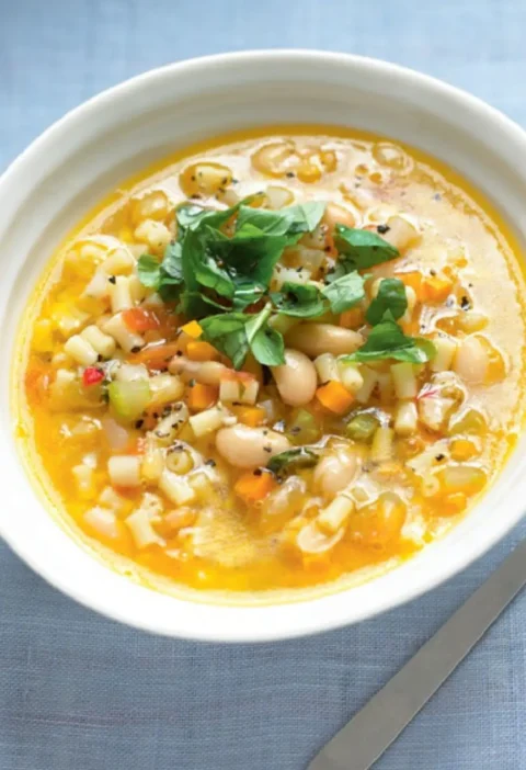 Bowl of peasant soup with cannellini beans, diced vegetables, small pasta and shredded basil on top