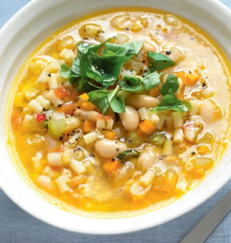 Bowl of peasant soup with cannellini beans, diced vegetables, small pasta and shredded basil on top