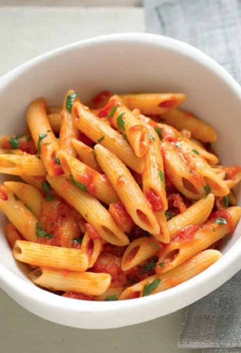 Penne with chili sauce and chopped parsley in a white bowl