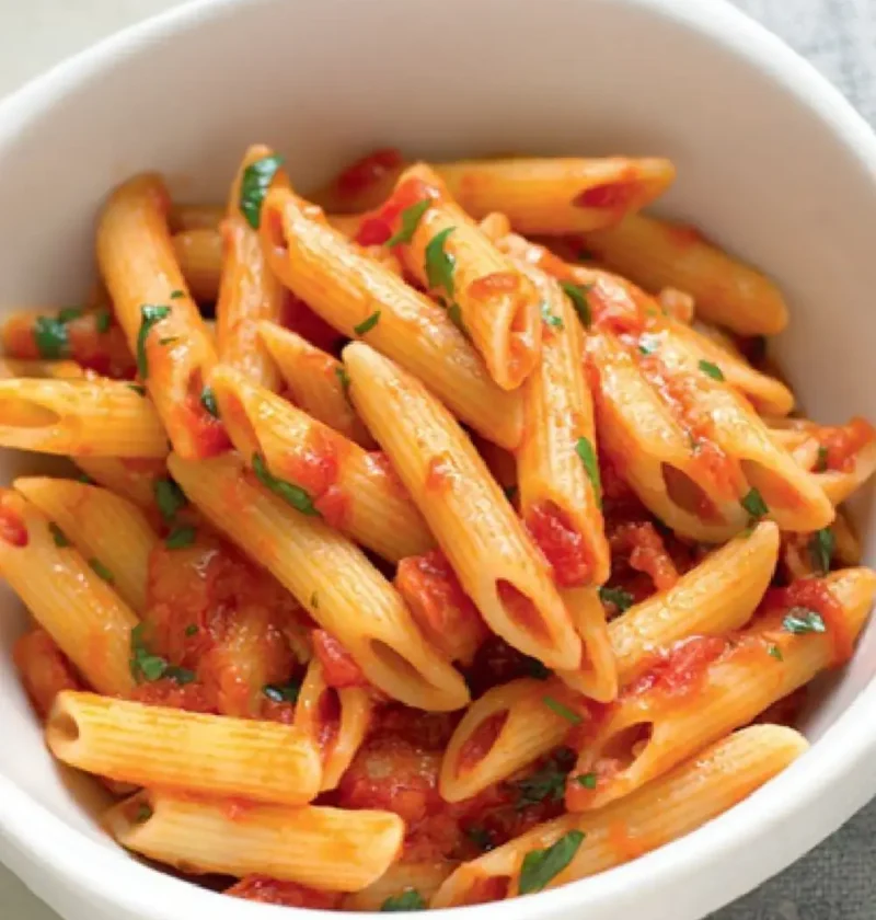 Penne with chili sauce and chopped parsley in a white bowl