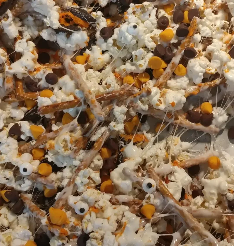 Popcorn Halloween mix with pretzel sticks, Oreo pieces, orange and chocolate chips and candy eyeballs in marshmallow on a baking sheet