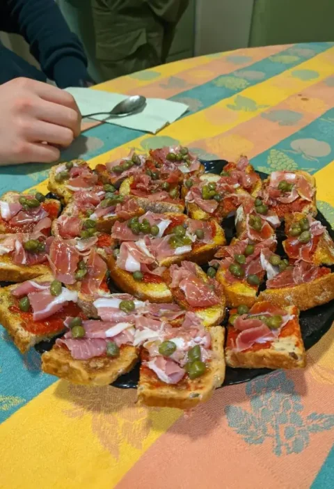 Platter of prosciutto wrapped appetizers: toasts topped with tomato, folded prosciutto and capers