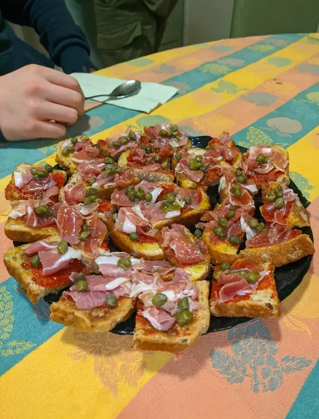 Platter of prosciutto wrapped appetizers: toasts topped with tomato, folded prosciutto and capers