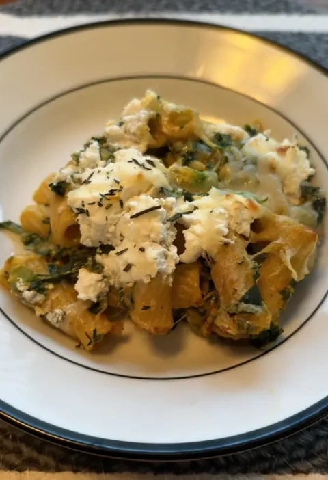 Pumpkin baked mac and cheese with kale and melted ricotta on a plate, topped with fresh herbs