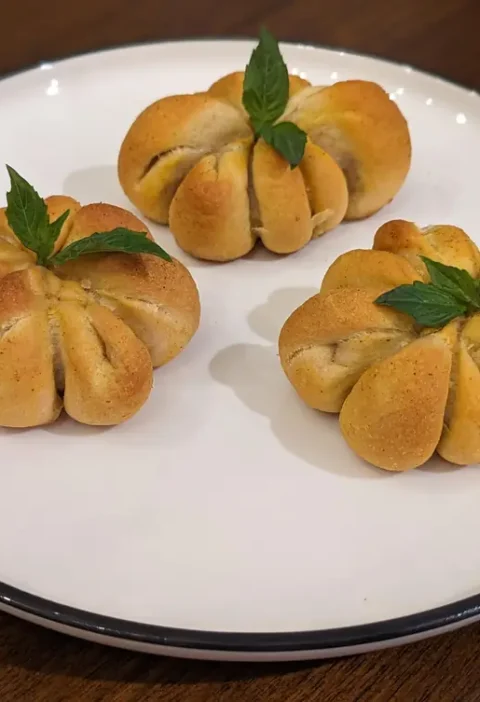 Three pumpkin pizza bites shaped like mini pumpkins with basil leaf stems on a white plate