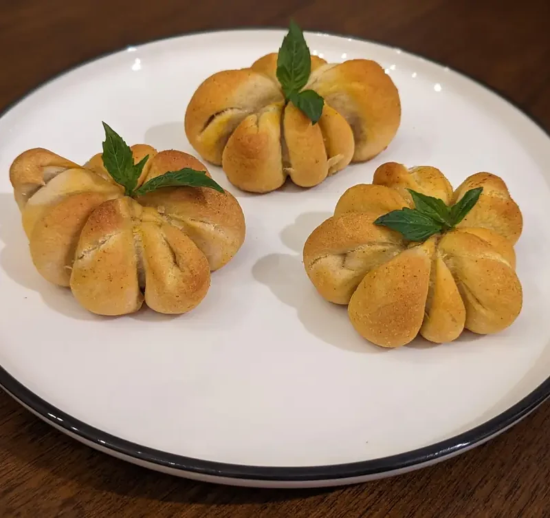 Three pumpkin pizza bites shaped like mini pumpkins with basil leaf stems on a white plate