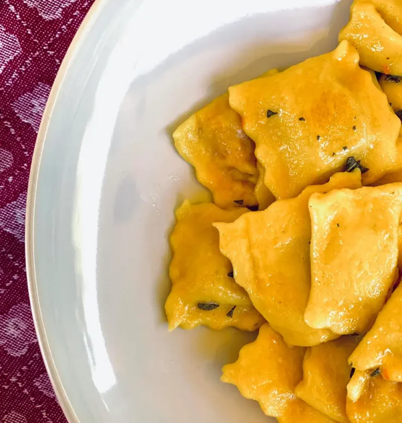 Pumpkin tortelli with sage butter in a pale bowl on a burgundy cloth