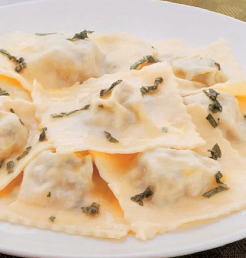 Ravioli with spinach and ricotta on a white plate, topped with chopped sage and butter