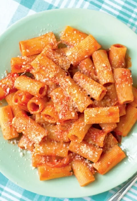 Rigatoni with pork ragout topped with grated Parmesan on a pale green plate
