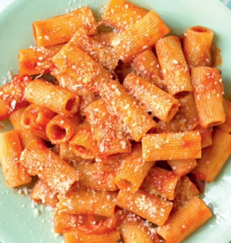 Rigatoni with pork ragout topped with grated Parmesan on a pale green plate