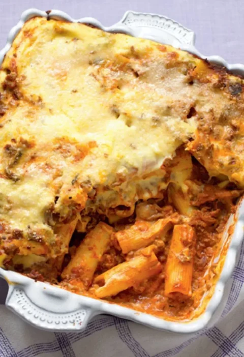 Baked rigatoni with rich Bolognese sauce in a white dish with a golden cheese top and pasta showing below
