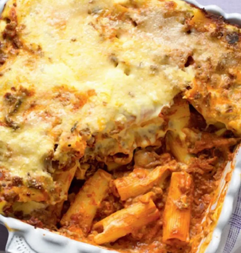 Baked rigatoni with rich Bolognese sauce in a white dish with a golden cheese top and pasta showing below