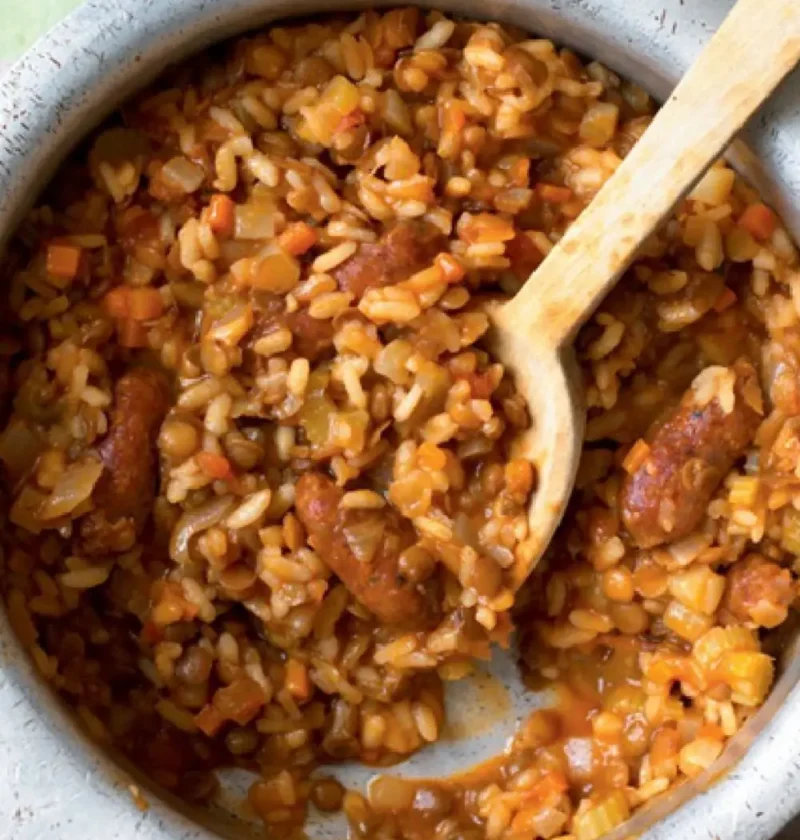 Risotto with lentils and sausages in a gray pot with a wooden spoon