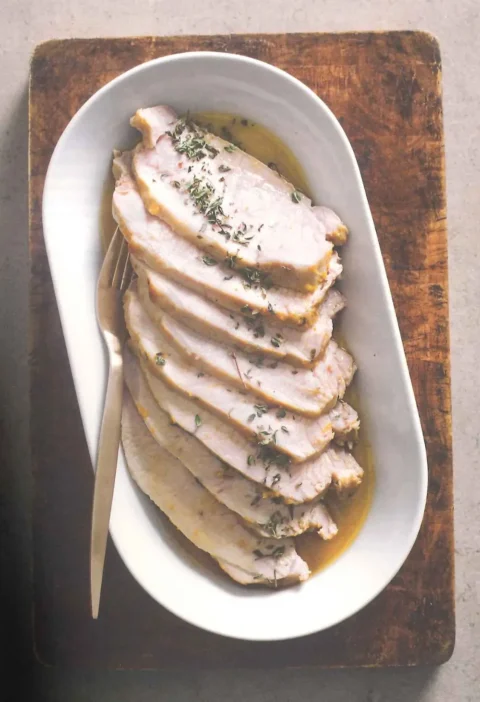 Sliced roasted pork loin with fresh thyme and cooking juices on a white oval serving dish