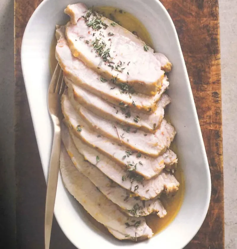 Sliced roasted pork loin with fresh thyme and cooking juices on a white oval serving dish