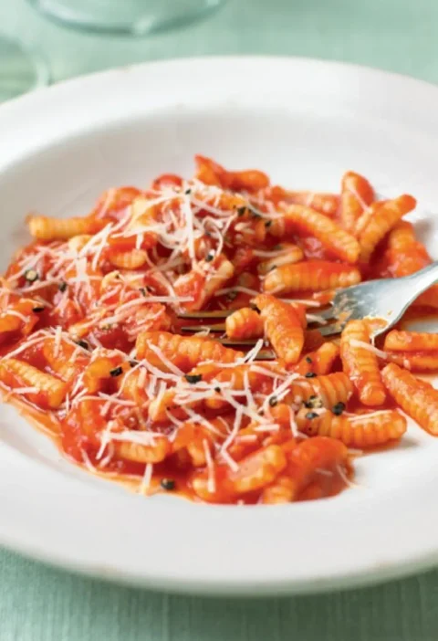 Sardinian gnocchi with tomato sauce in a white bowl, topped with grated pecorino and basil