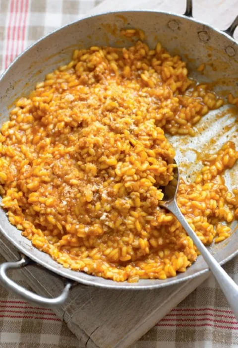 Sardinian risotto in a metal pan with a spoon, orange saffron and tomato rice topped with grated cheese