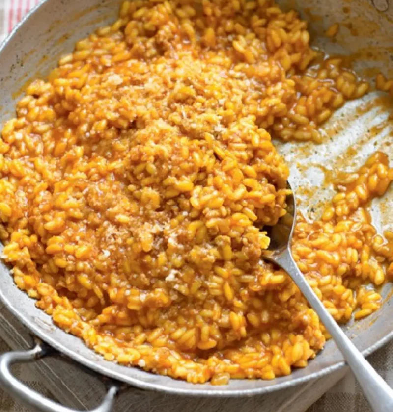 Sardinian risotto in a metal pan with a spoon, orange saffron and tomato rice topped with grated cheese
