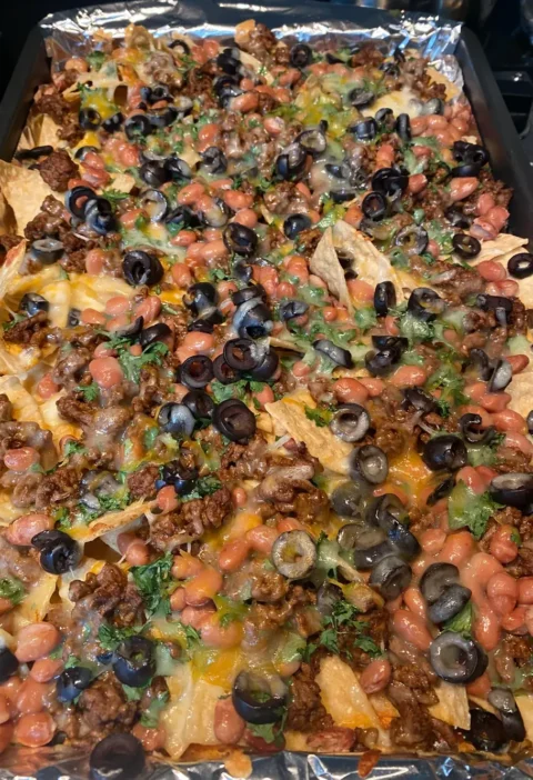 Sheet pan halloween nachos on a foil-lined baking sheet topped with ground beef, melted cheese, black olives and cilantro
