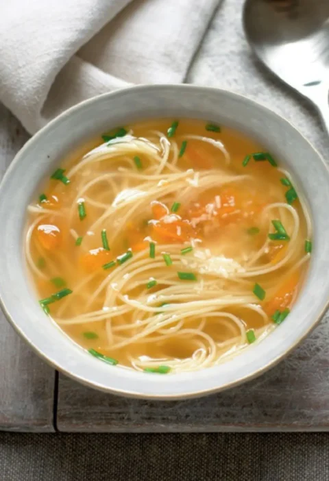 Bowl of soup with pasta, chicken broth, diced tomato and chopped chives