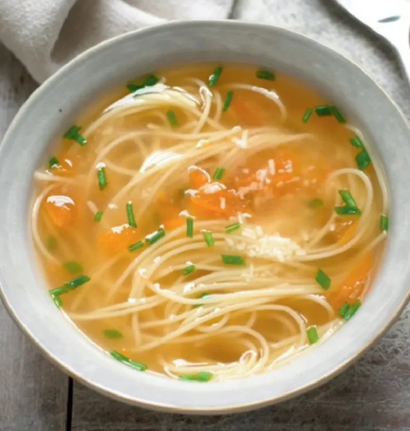 Bowl of soup with pasta, chicken broth, diced tomato and chopped chives
