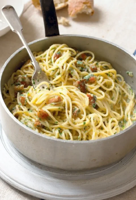 Spaghetti carbonara with pancetta and parsley in a metal pot with a fork