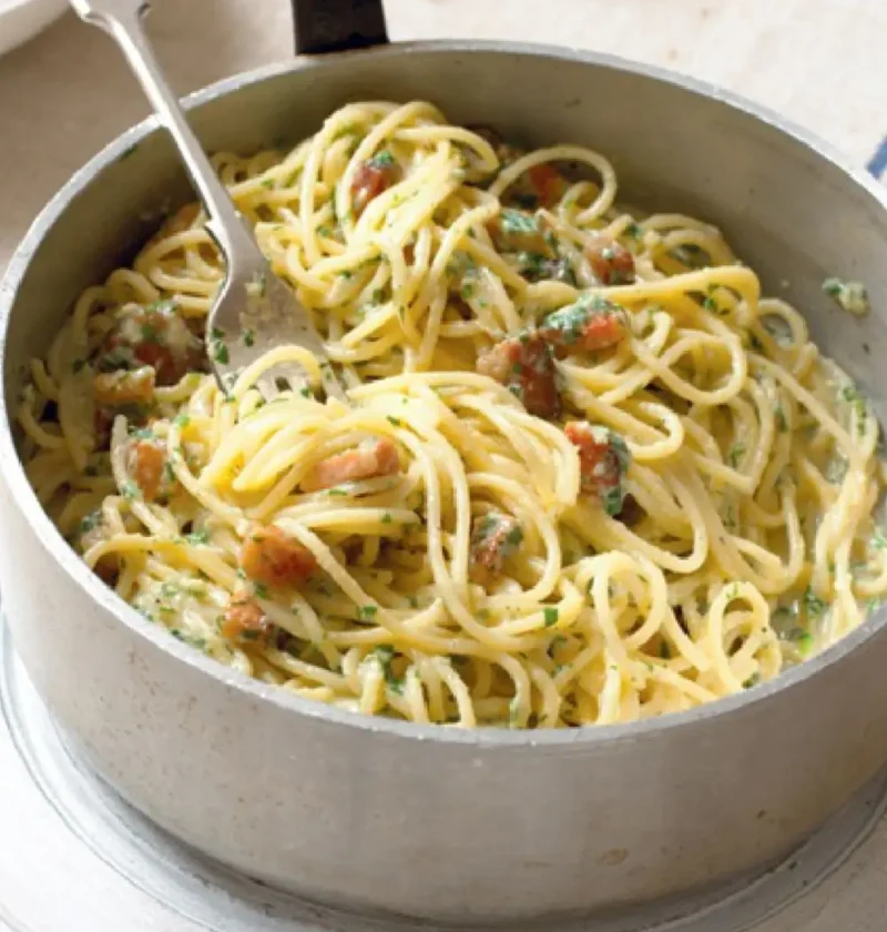 Spaghetti carbonara with pancetta and parsley in a metal pot with a fork
